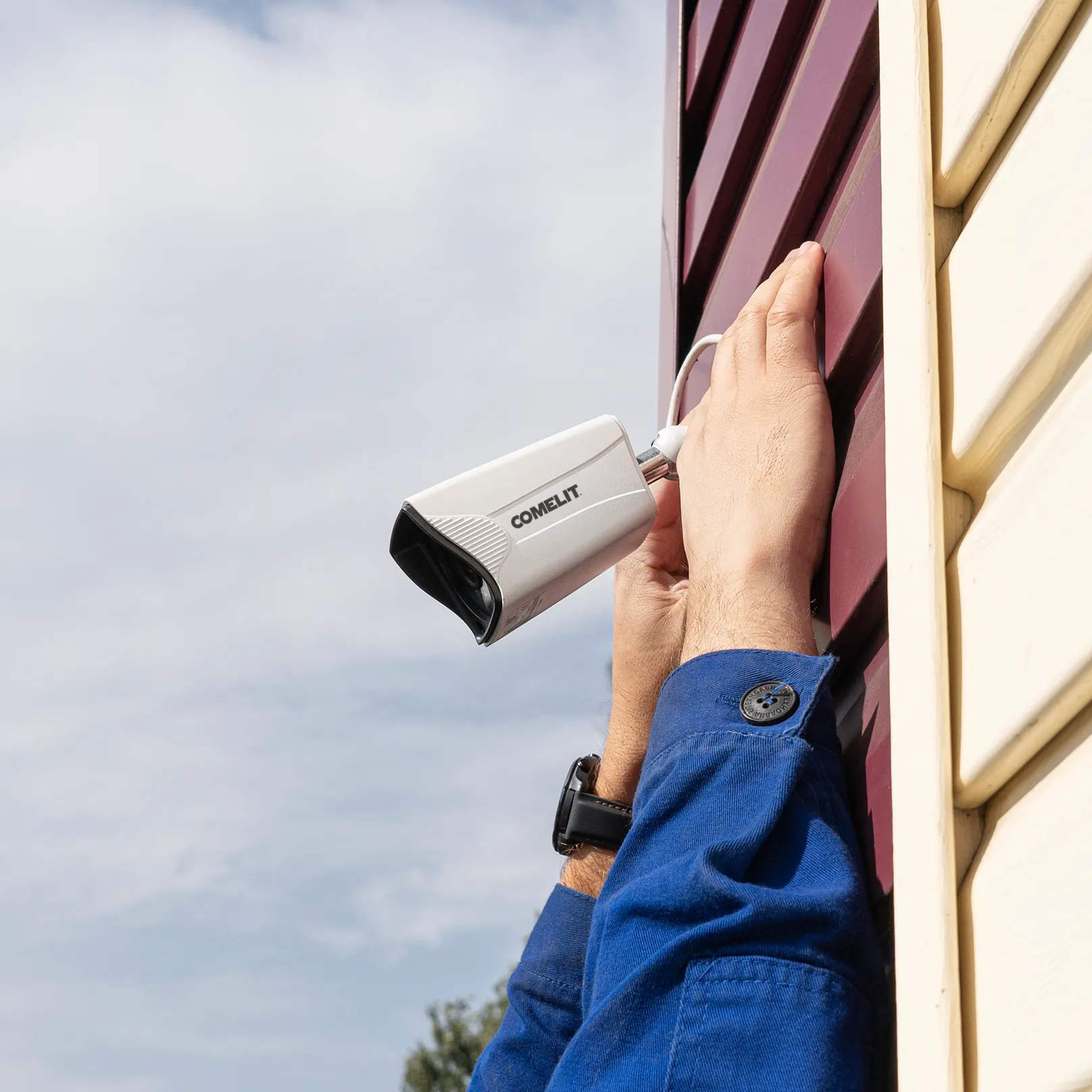 Installateur fixant une caméra de surveillance Comelit sur une façade extérieure.
